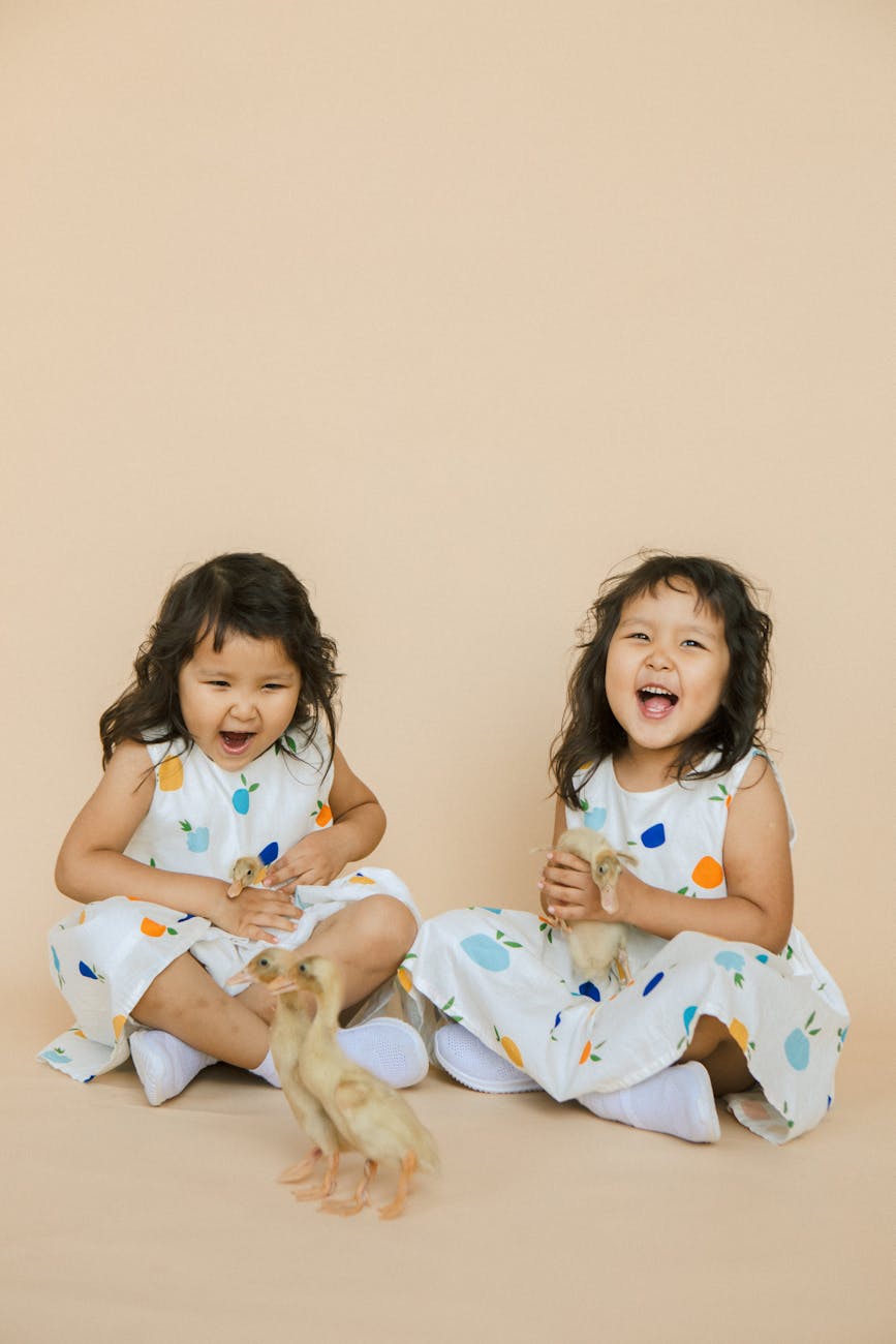 twin girls sitting holding ducklings and smiling